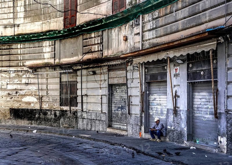 A man sits in front of a closed shop in the historic centre of Naples, 02/05/2024, Naples, Italy, Europe