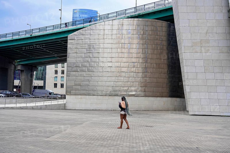 Guggenheim Museum Bilbao on the banks of the river Nervion, Architect Frank O. Gehry, Bilbao, A woman walks under a paved area next to a modern bridge and metallic buildings. The atmosphere is urban and lonely, Guggenheim Museum, Architect Frank O. Gehry, Bilbao, Province of Bizkaia, Basque Country, Spain, Europe