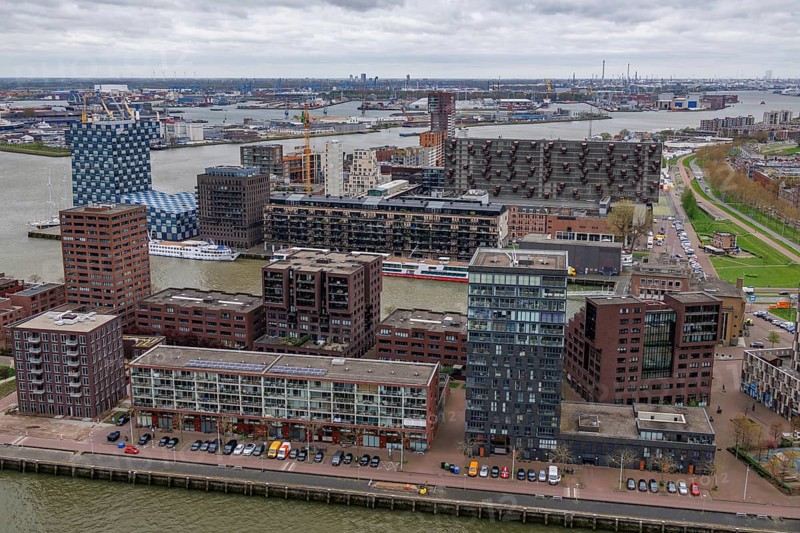 Modern residential complexes and buildings line the riverbank, shaping the urban architecture under a grey sky, modern houses and a bridge with a river from above, Rotterdam, Netherlands