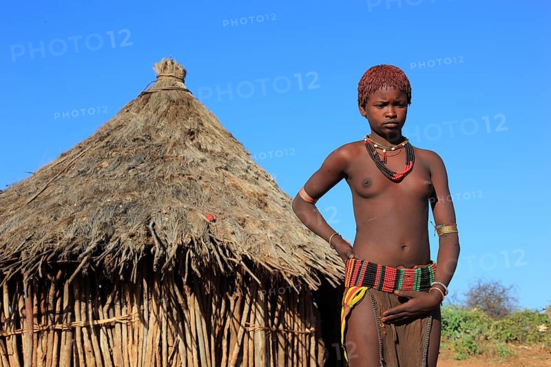 South Ethiopia, Omo region, young woman of the Hammer people standing in front of a round hut, dwelling, Ethiopia, Africa