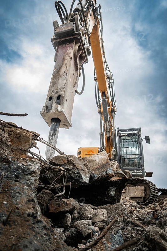 An excavator on a construction site working on a pile of rubble, large pieces of metal next to it, grey cloudy sky, demolition, Saarbruecken, Germany, Europe