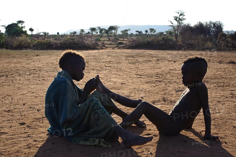 Boys from the Hamer tribe, one is removing a thorn in the foot of the other one, Omo valley, ethiopia