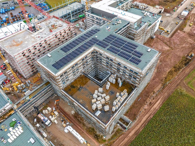 Construction site with buildings in shell construction and installed solar panels, stored building materials, surrounded by rural environment, construction site of new hospital, Calw Black Forest Germany