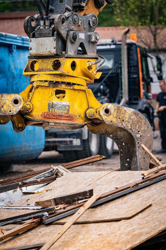 An excavator with a hydraulic grab stacks wood debris while a worker stands nearby, demolition, Saarbruecken, Germany, Europe