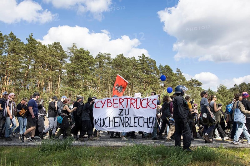 Participants with banners Cybertrucks to cake tins at the demonstration Water. Forest. Justice against the expansion of the Tesla Gigafactory in Gruenheide near Berlin, 11.05.2024