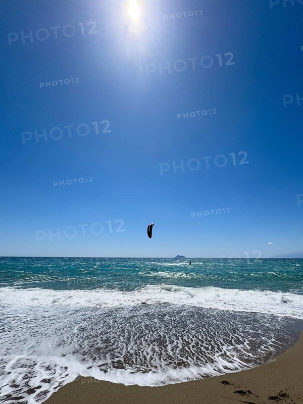 Kitesurfer kite surfer surfing in strong wind and waves rough sea moving sea with inflated sail, in foreground outgoing wave on beach, Kalamaki, Crete, Greece, Europe