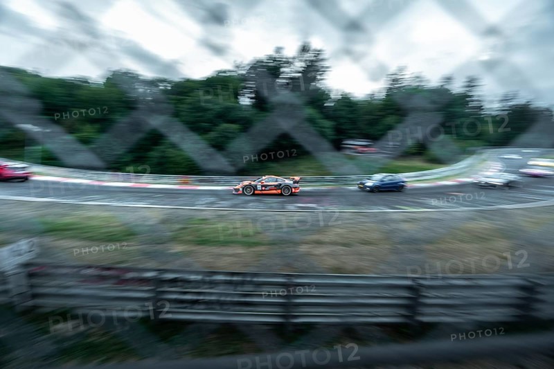 A racing car in action, captured with motion blur and visible through a fence. Nuerburgring race track, Nuerburg Germany