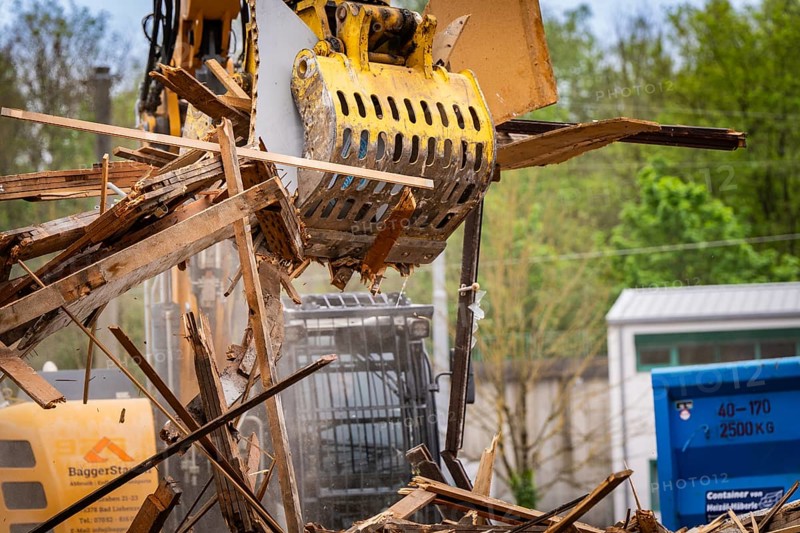 An excavator above a blue container lifts wood waste on a construction site, demolition, Saarbruecken, Germany, Europe