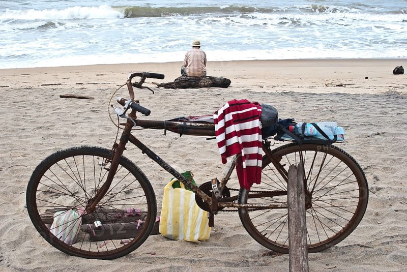 Old man fishing on the beach, looking the Indian ocean, Mananjary, Madagascar. In the foreground, the bicycle of the old man