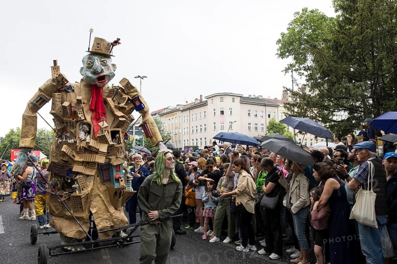 Sculpture by the Artistania group next to spectators with umbrellas at the street parade of the 26th Carnival of Cultures in Berlin on 19 May 2024