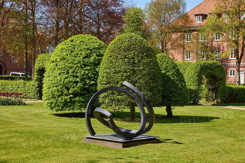 Art object and european hornbeams (Carpinus betulus) with topiary in the Marktstrasse park in Niebuell, Nordfriesland district, Schleswig-Holstein, Germany, Europe