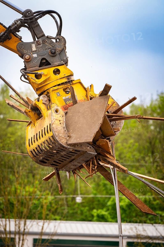 Large yellow hydraulic grab on an excavator lifting pieces of wood, with green background, demolition, Saarbruecken, Germany, Europe