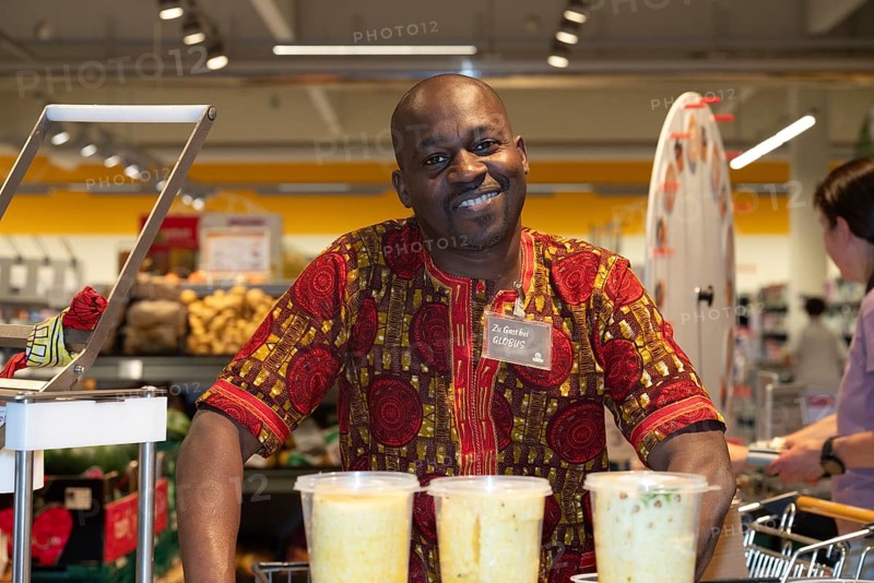 A man from Ivory Coast, black skin colour, wearing a traditional African shirt, smiling behind a sales stand in a Globus supermarket, pineapple seller, Plattling, Bavaria, Germany, Europe