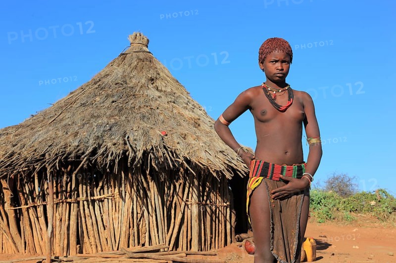South Ethiopia, Omo region, young woman of the Hammer people standing in front of a round hut, dwelling, Ethiopia, Africa