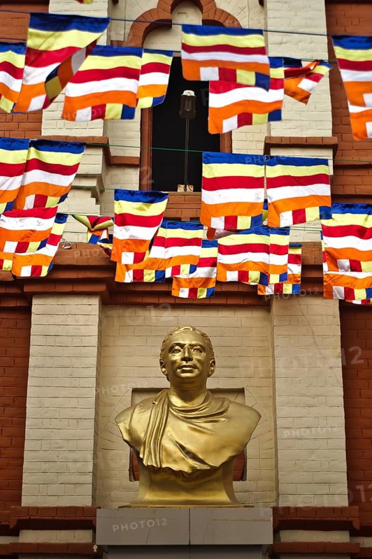 Statue representing Anagarika Dharmapala, the sri lankan founder of the Mahabodhi society of India, Bodhgaya, Bihar, India. Buddhist flags on the top