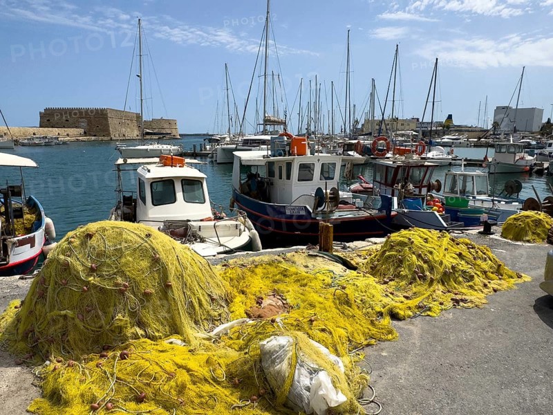 In the foreground yellow fishing nets of local Greek fishermen behind them several small fishing boats, in the background historical fortress built in the Middle Ages 16th century by Republic of Venice old name Castello Rocca al Mare today Koules in harbour of Iraklion, Heraklion, Crete, Greece, Europe