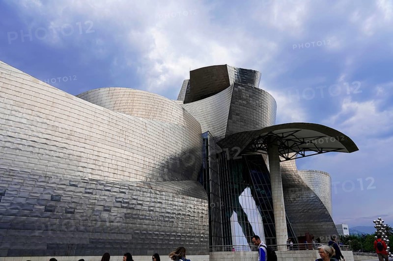 Guggenheim Museum Bilbao on the banks of the river Nervion, architect Frank O. Gehry, Bilbao, people in front of the modern art museum with its curved metal facade and cloudy sky. The atmosphere is lively and art-orientated, Guggenheim Museum, architect Frank O. Gehry, Bilbao, province of Bizkaia, Basque Country, Spain, Europe