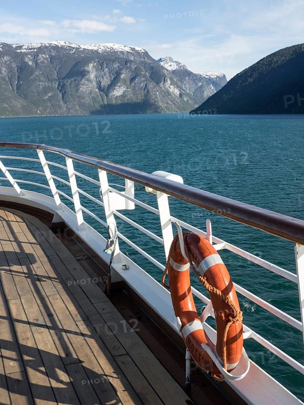 View from a ship on a calm fjord with snow-covered mountains in the background and a life belt on the railing, cruise through the norwegian fjords with impressive mountains and green trees, Flam, norway