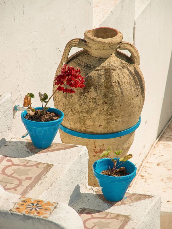 A large clay jug and two blue flower pots with plants adorn a rustic Mediterranean-style staircase, Tunis in Africa with ruins from Roman times, modern mosques and blue and white houses in sidi-bou-said, Tunis, Tunisia, Africa