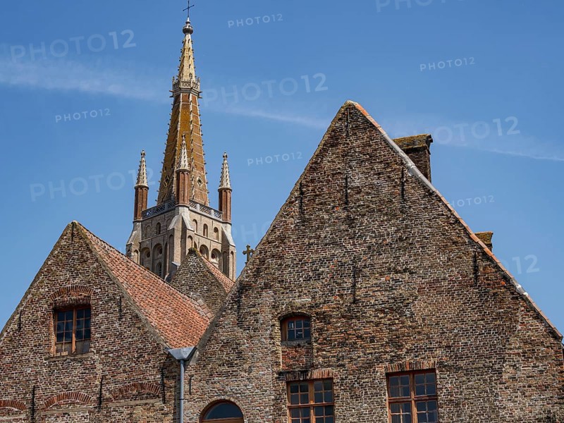 Old brick buildings with gothic tower in the background under a bright blue sky, historic city on the river with ornate gables, old facades and historic towers, Bruges, Belgium, Europe