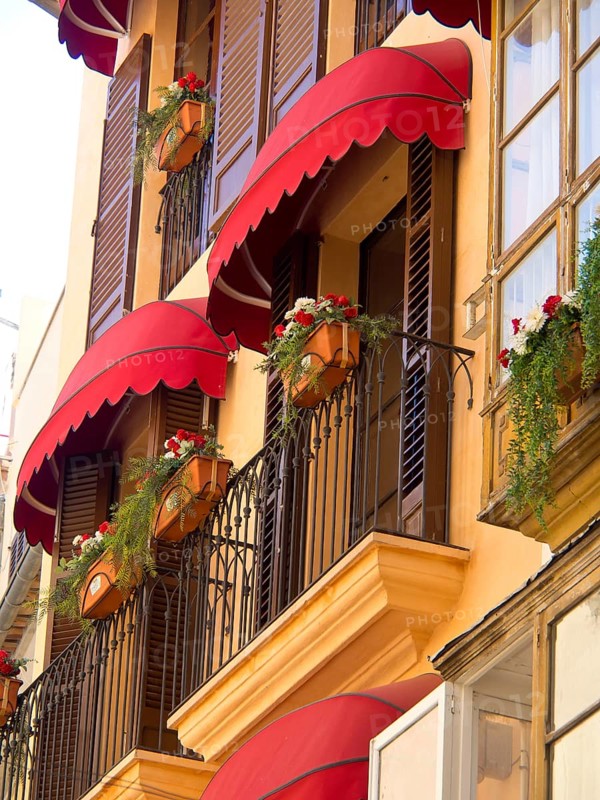 Buildings with red awnings, flowers and decorative balconies, palma de Majorca with its historic houses, the great cathedral and flowers, palma, spain