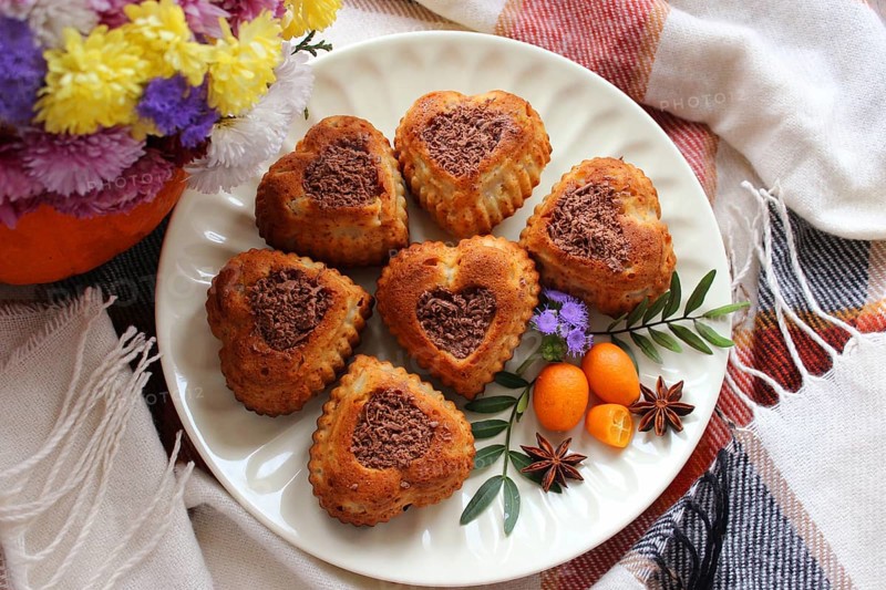 Heart-shaped cookies with chocolate shavings arranged on a plate with flowers, kumquats, and star anise, set on a plaid cloth