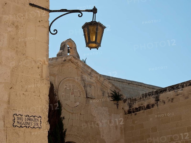 Historic street with a lantern and old beige stone buildings under a clear blue sky, Historic buildings with beautiful windows, balconies and small towers, Mdina, Malta, Europe