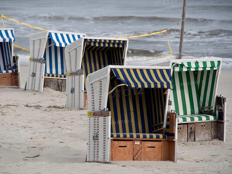 Several empty beach chairs with striped awnings stand on the beach near the sea, a volleyball net in the background, beach chairs on the sandy beach of Wangerooge on the North Sea, Wangerooge, germany