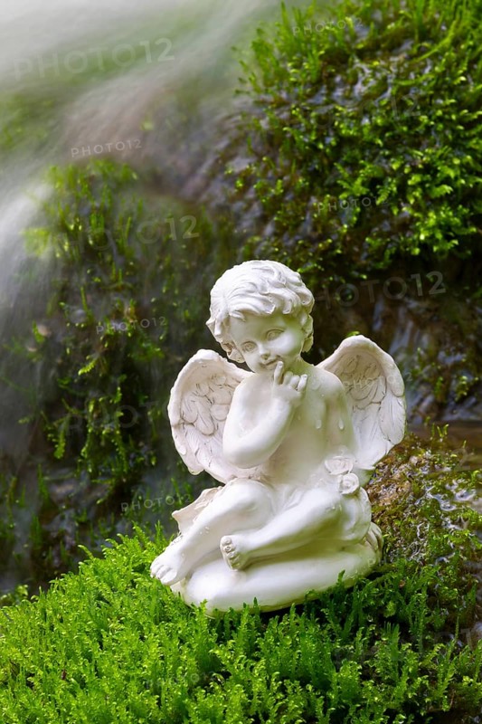 Porcelain angel figurine on moss by a waterfall
