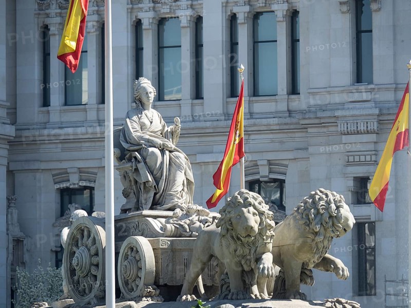 Historic fountain with a statue and two lions flanked by Spanish flags, Madrid, Spain, Europe