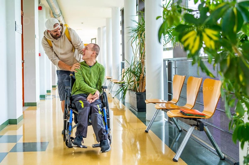 Disabled man with wheelchair and friend walking along in the university corridor