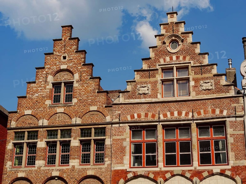 Brick architecture with magnificent stepped gables and windows silhouetted against a blue sky, medieval facades with historic churches and buildings in a riverside town, Ghent, Belgium, Europe