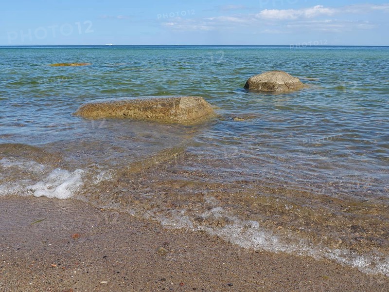 Clear sea water gently meets stones on the beach under a sunny, blue sky, spring on the Baltic Sea beach in Poland with green trees, sopot, poland
