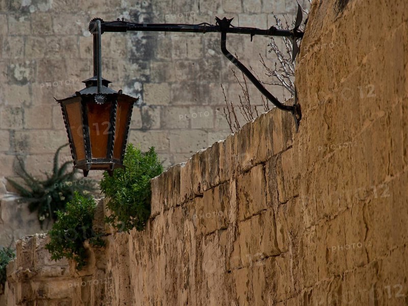 Old lantern on a traditional stone wall with some vegetation, the village of mdina on the island of malta with historic houses, colourful balconies, magnificent churches, mdina, Malta, Europe