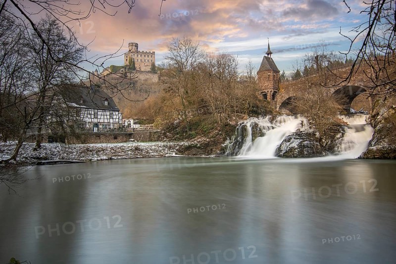 Beautiful landscape in winter with ice and snow. Waterfall of the river Elz near the castle Pyrmont, the country inn Pyrmonter Muehle directly at a lake. A historic bridge in Rhineland-Palatinate, Germany, Europe