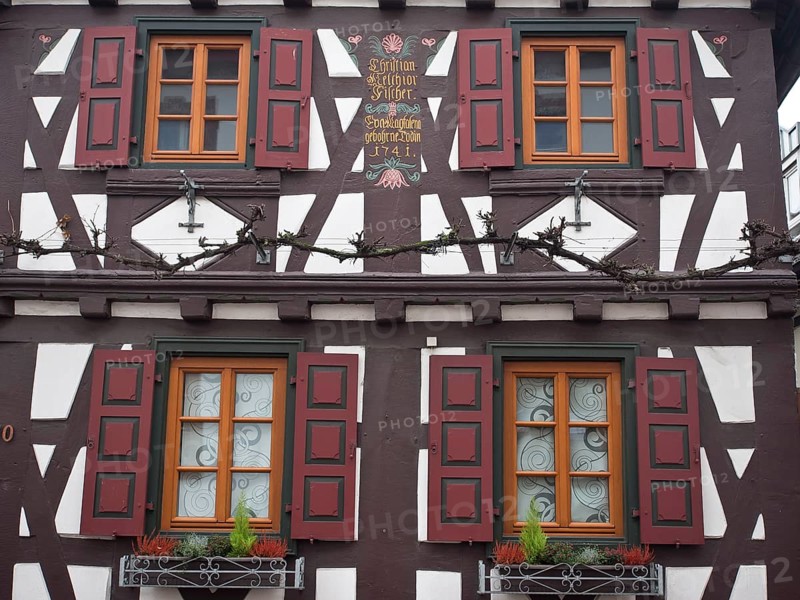 Detail of a half-timbered house with red shutters and decorative flowers on the window, kandel, germany