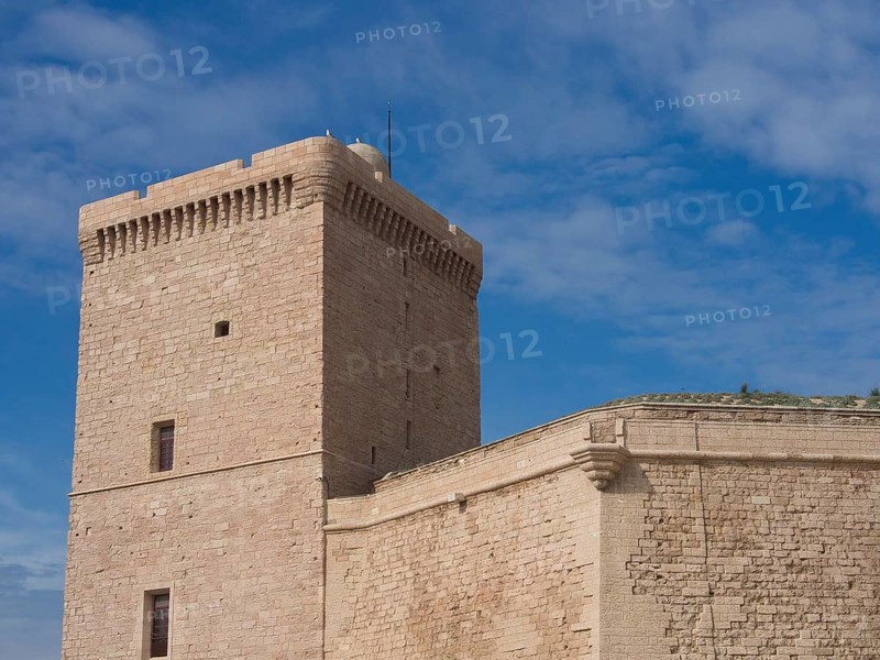 Historic stone tower of a fortress under a slightly cloudy blue sky, Marseille on the Mediterranean Sea with the old cathedral and ships in the historic harbour, rocky coast on the Mediterranean Sea, marseille, france