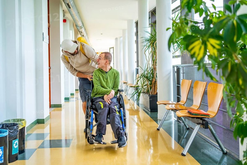 Friend pushing the wheelchair of a disabled man with cerebral palsy in the university