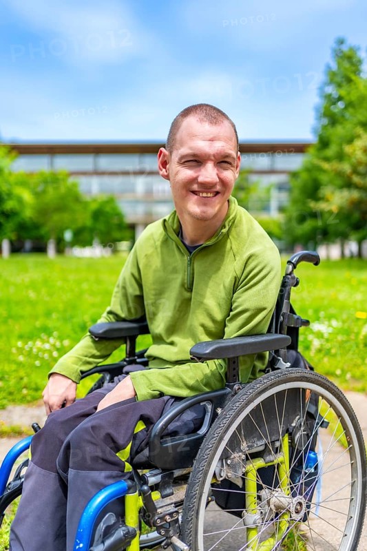 Close-up portrait of a happy disabled man in the university campus sitting in wheelchair smiling at camera