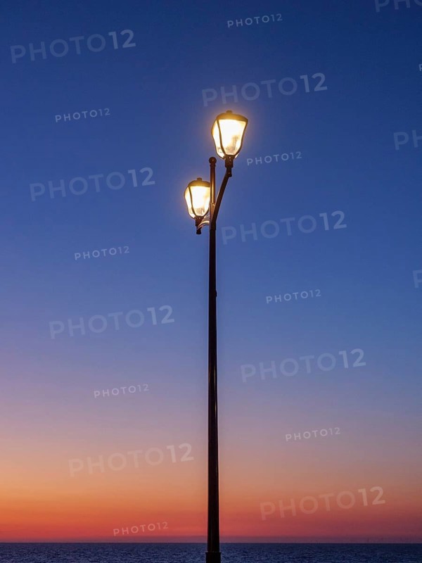 An illuminated street lamp in front of an orange sky at sunset, sunset in many colours on the beach with a calm sea, de haan, belgium