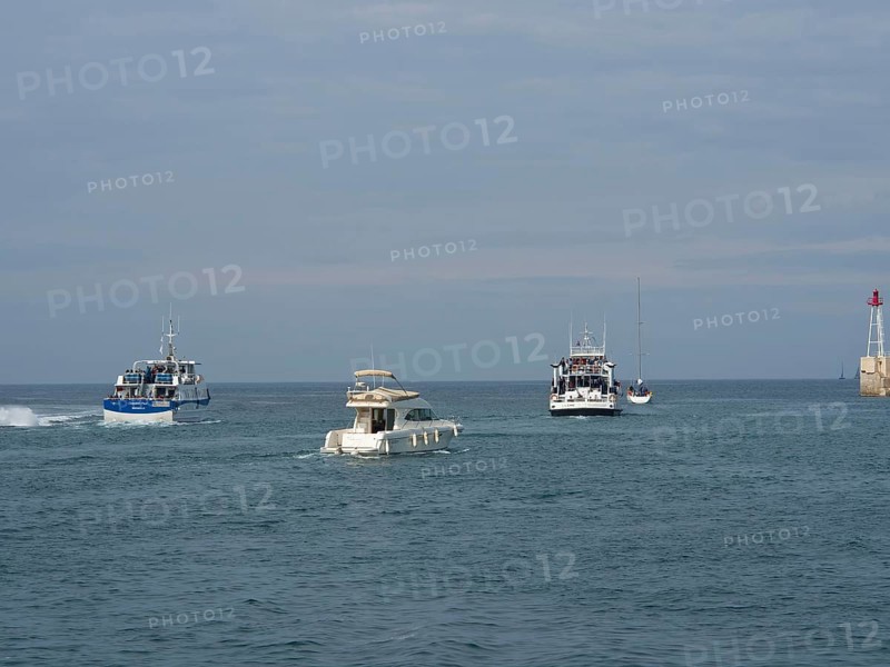 Boats sailing on the sea towards a harbour, accompanied by the wide sky and a lighthouse in the distance, Marseille on the Mediterranean Sea with the old cathedral and ships in the historic harbour, rocky coast on the Mediterranean Sea, marseille, france
