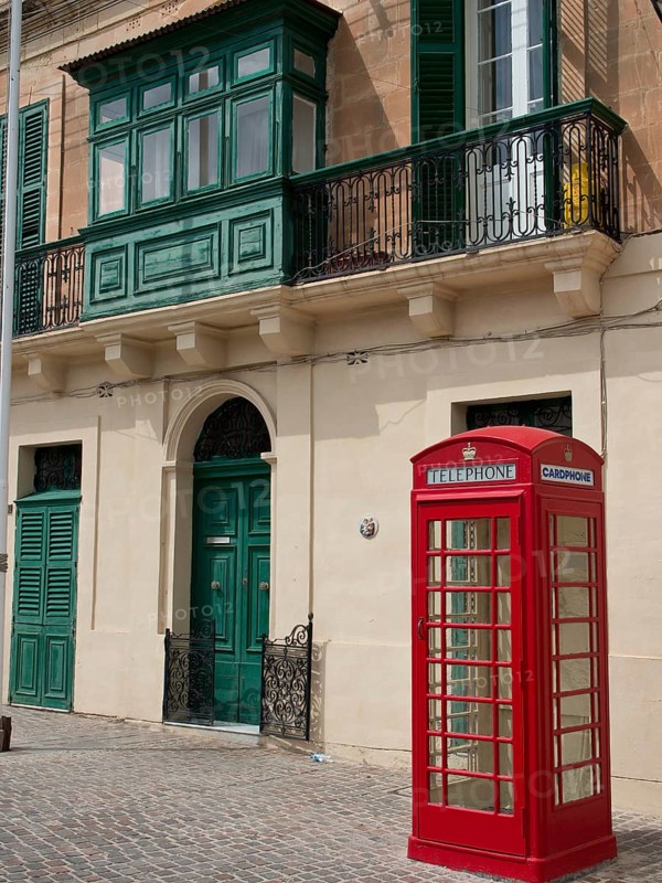 Red telephone box in front of a building with green shutters and decorative balconies, Valetta, Malta, Europe