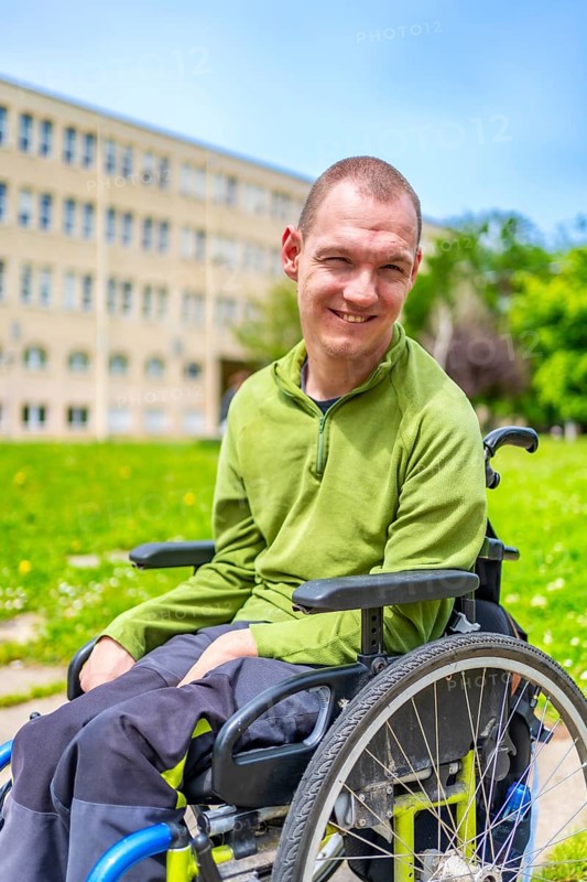 Vertical close-up portrait of a man with cerebral palsy smiling in wheelchair in the university campus