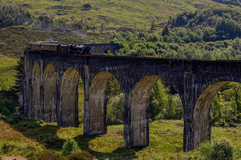 An old train crosses an impressive stone viaduct bridge stretching over a wooded glen under a clear sky, Scotland, United Kingdom, Europe