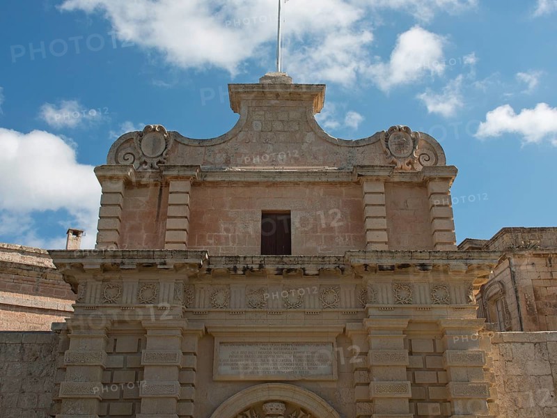 Entrance of a historic building with decorated stone archway under blue sky with clouds, the town of mdina on the island of malta with historic houses, colourful balconies, magnificent churches, mdina, Malta, Europe
