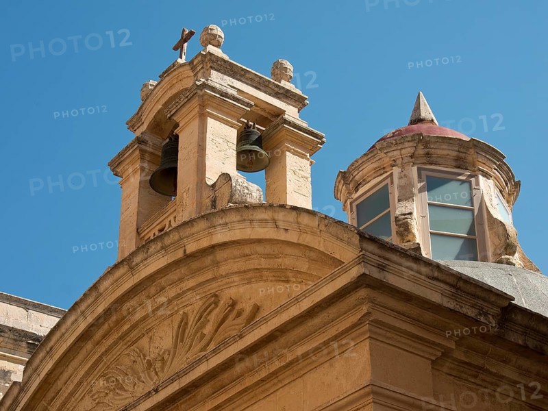 A building of an old church with bells and round windows under a blue sky, the town of mdina on the island of malta with historic houses, colourful balconies, magnificent churches, mdina, Malta, Europe