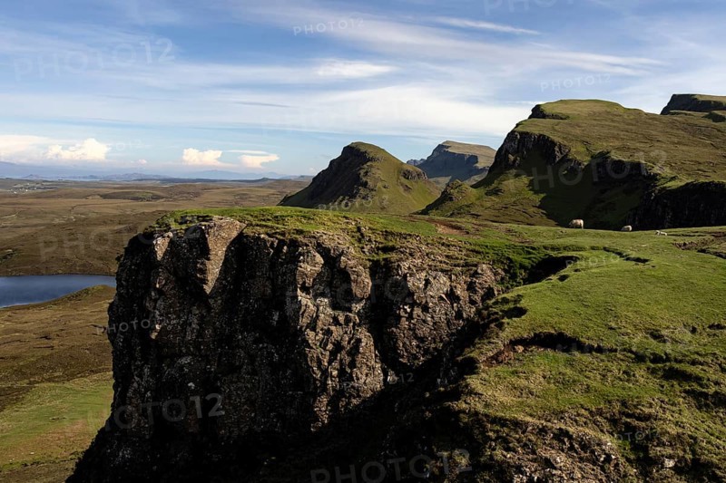 Dramatic cliffs and green slopes in an expansive mountain landscape under a blue sky with scattered white clouds, Quiraing