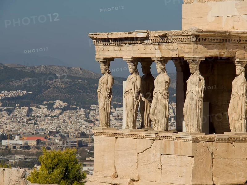 Ancient columns with caryatid sculptures and a cityscape in the background, ancient columns in front of a blue sky, athens, greece