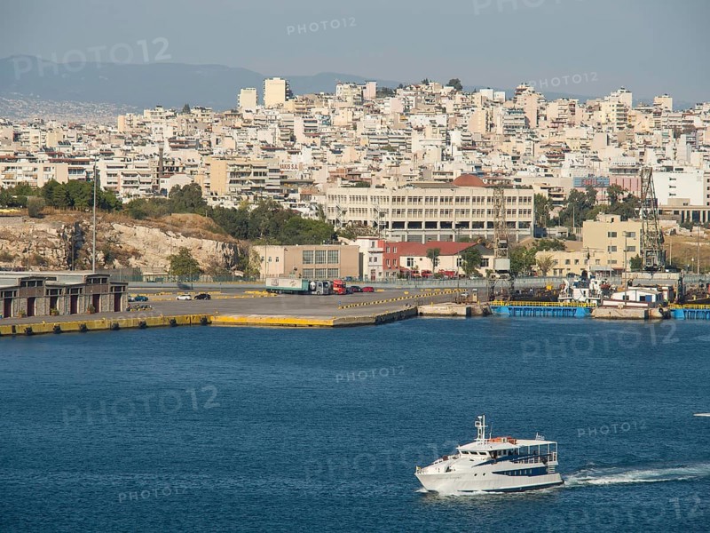 A boat sails in the harbour, in the background numerous buildings of the city, Ancient buildings with columns and trees on the Acropolis in Athens against a blue sky, athens, greece