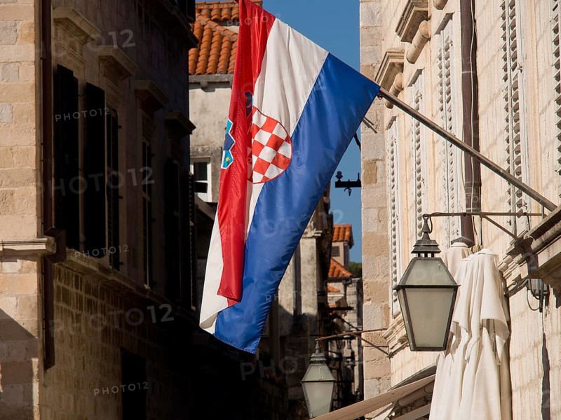 Croatian flag waving in a narrow alley with historic buildings and alleyway lamps, the old town of Dubrovnik with historic houses, churches, red roofs and fortress walls, dubrovnik, coratia